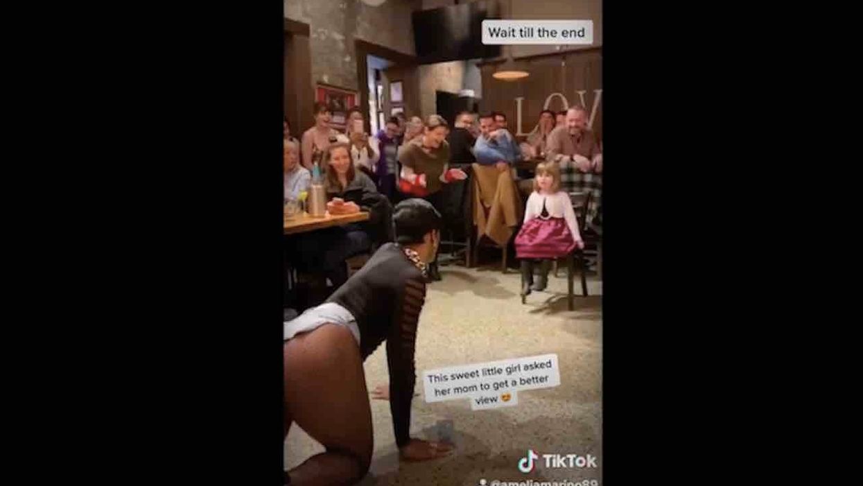 Drag queen performs suggestive dance for little girl — crawls up to her on hands and knees — while adults in room smile, clap, shimmy